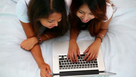beautiful happy sisters lying on bed using laptop