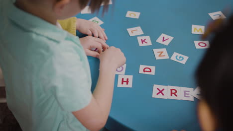 primo piano degli alunni seduti alla scrivania rotonda e che giocano con le lettere dell'alfabeto in una scuola montessori 1