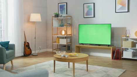 cozy living room with stylish furniture and design, green chroma key tv in the middle of the room. zoom in camera shot.