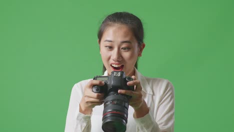 close up of asian photographer saying wow after looking at the pictures in the camera while standing on green screen background in the studio