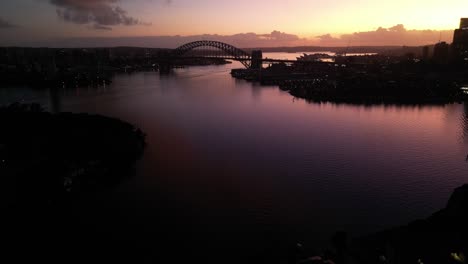 Atemberaubender-Sonnenaufgang-Am-Hafen-Von-Sydney-Mit-Der-Hafenbrücke-Und-Dem-Opernhaus-Im-Hintergrund