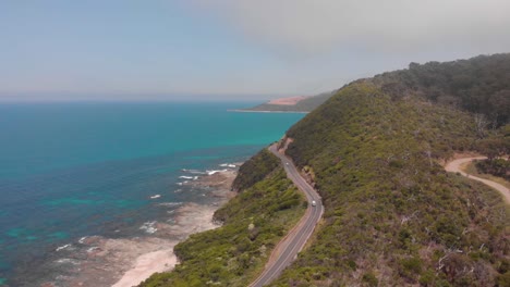 high-aerial-reveal-over-hills-showing-car-travelling-down-picturesque-coastal-road