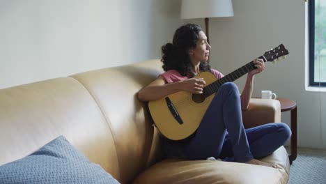 Glückliche-Frau-Mit-Gemischter-Abstammung,-Die-Auf-Dem-Sofa-Sitzt-Und-Gitarre-Spielt