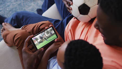 composite of father and son at home watching hockey match on smartphone