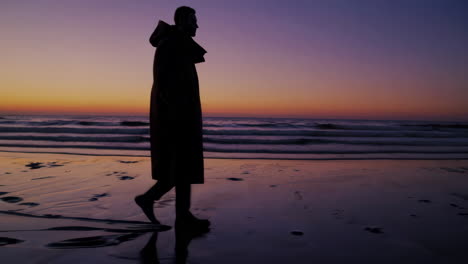 man die op het strand loopt bij zonsondergang