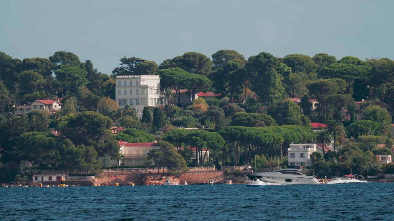 A motor yacht cruises along the coast lined with beautiful villas surrounded by green pine trees