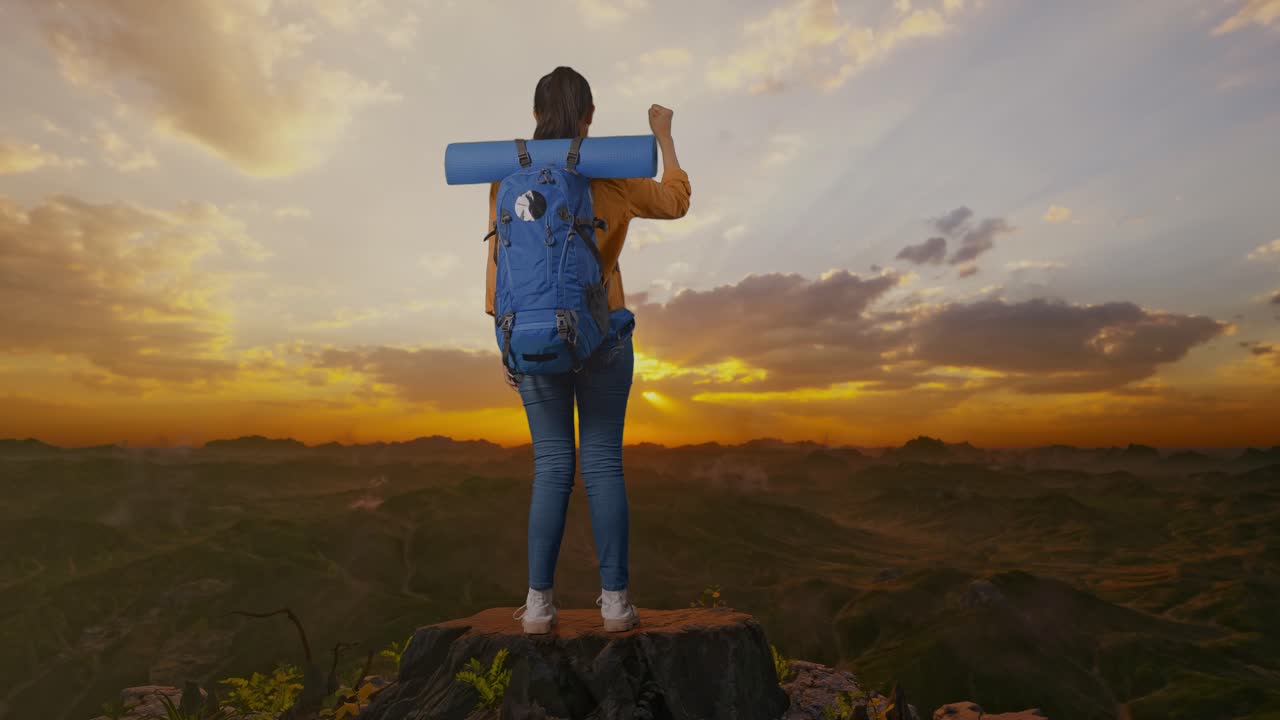 vista trasera del cuerpo completo de una excursionista femenina con mochila de montañismo gritando meta celebrando el éxito mientras estaba de pie en la cima de la montaña durante el atardecer