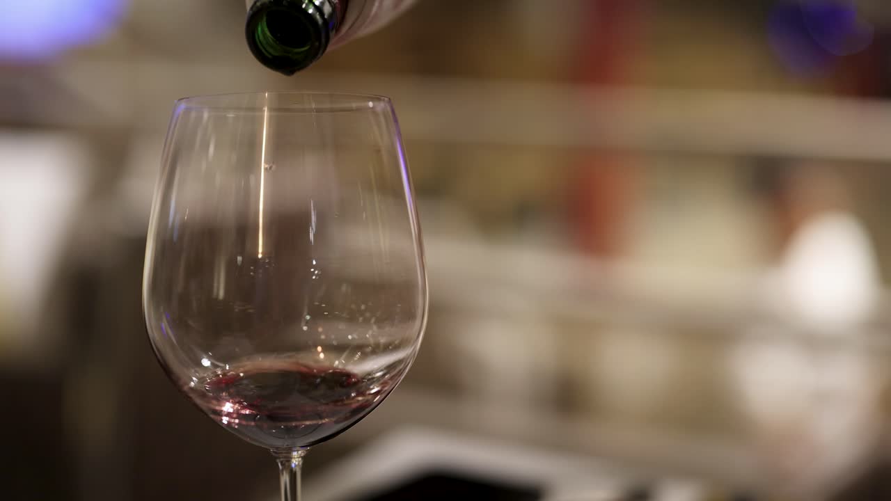 Una sequenza che mostra vino rosso versato in un bicchiere, evidenziando il flusso elegante e il colore intenso in un'ambientazione in penombra