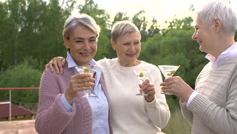 un grupo de tres mujeres mayores abrazándose y tomando una copa