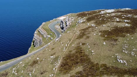 Scenic-green-rocky-moorland-mountain-country-road-overlooking-gorgeous-blue-Irish-sea-aerial-tilt-down