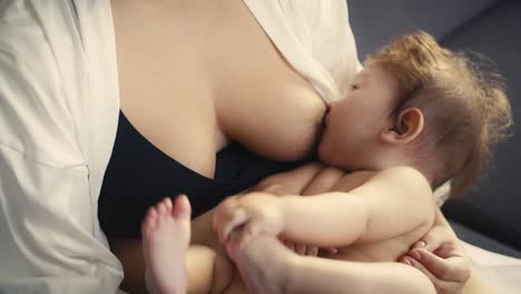 zoom out of asian baby breastfed by mother and playing with his legs