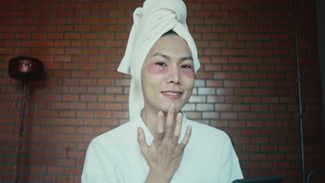 woman applying eye patches and facial mask