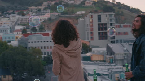 Amigos-Felices-Soplando-Burbujas-En-La-Azotea-Al-Atardecer-Disfrutando-De-Un-Fin-De-Semana-Sin-Preocupaciones-Con-El-Horizonte-Urbano-De-La-Ciudad-En-Segundo-Plano.