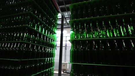 Multiple-stacks-of-green-glass-beer-bottles-in-factory-ready-to-be-filled-with-lager-pilsener,-mass-production-line