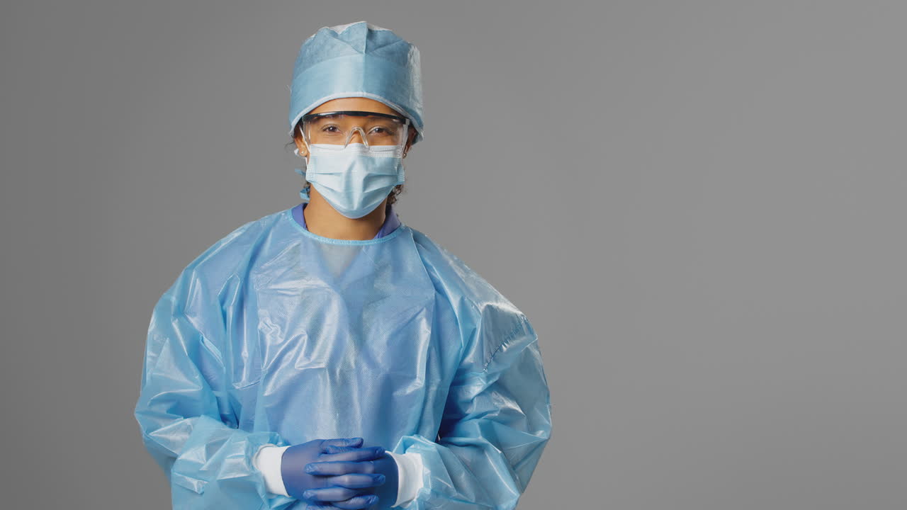 retrato de una cirujana sonriente con gafas de seguridad y máscara facial contra un fondo gris