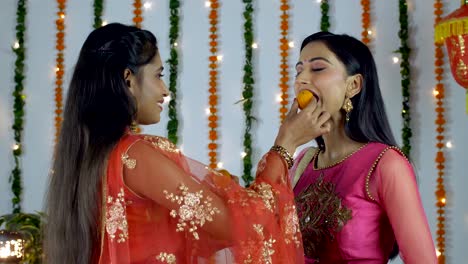 two indian females offering sweets to each other on the occasion of diwali/dipavali