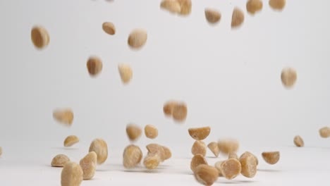 shelled macadamia nut pieces falling onto white table top and bouncing into a pile in slow motion