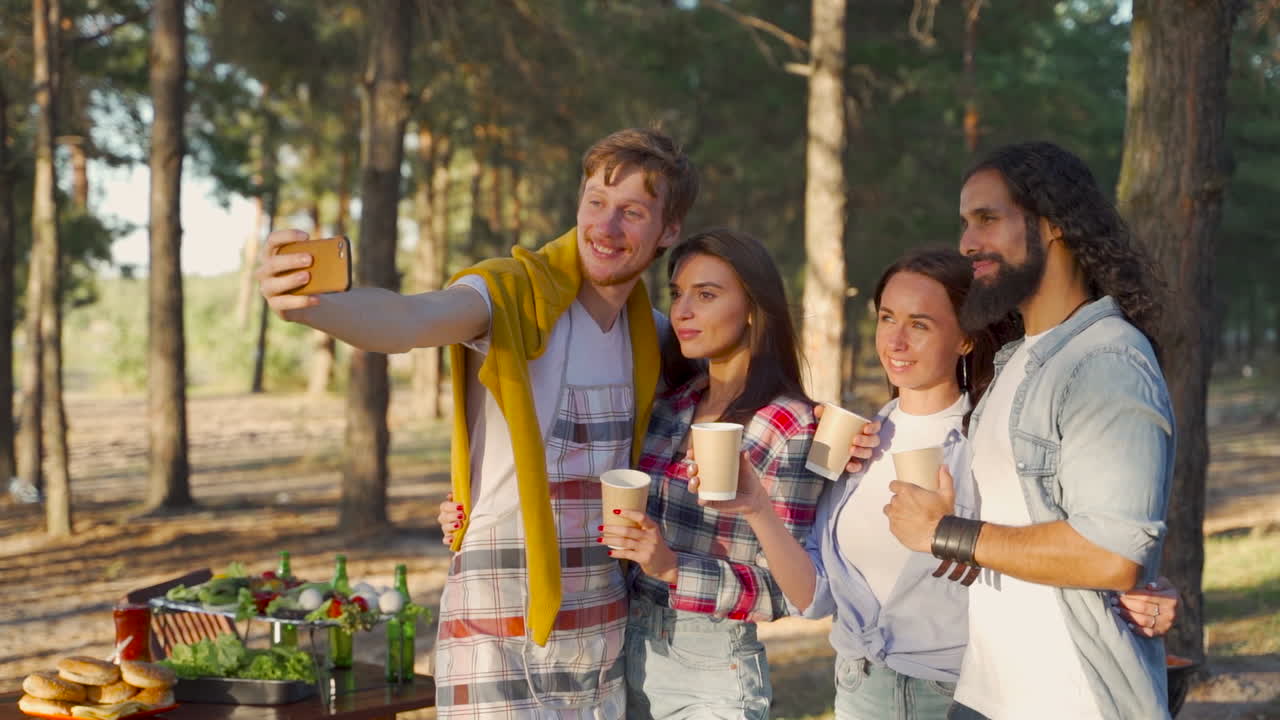 Young women and men taking a selfie with the phone. People enjoying a picnic in nature.
