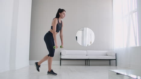 joven hermosa mujer morena de pie en una pierna haciendo curvas con pesas. realizando levantamiento muerto con pesas en casa.