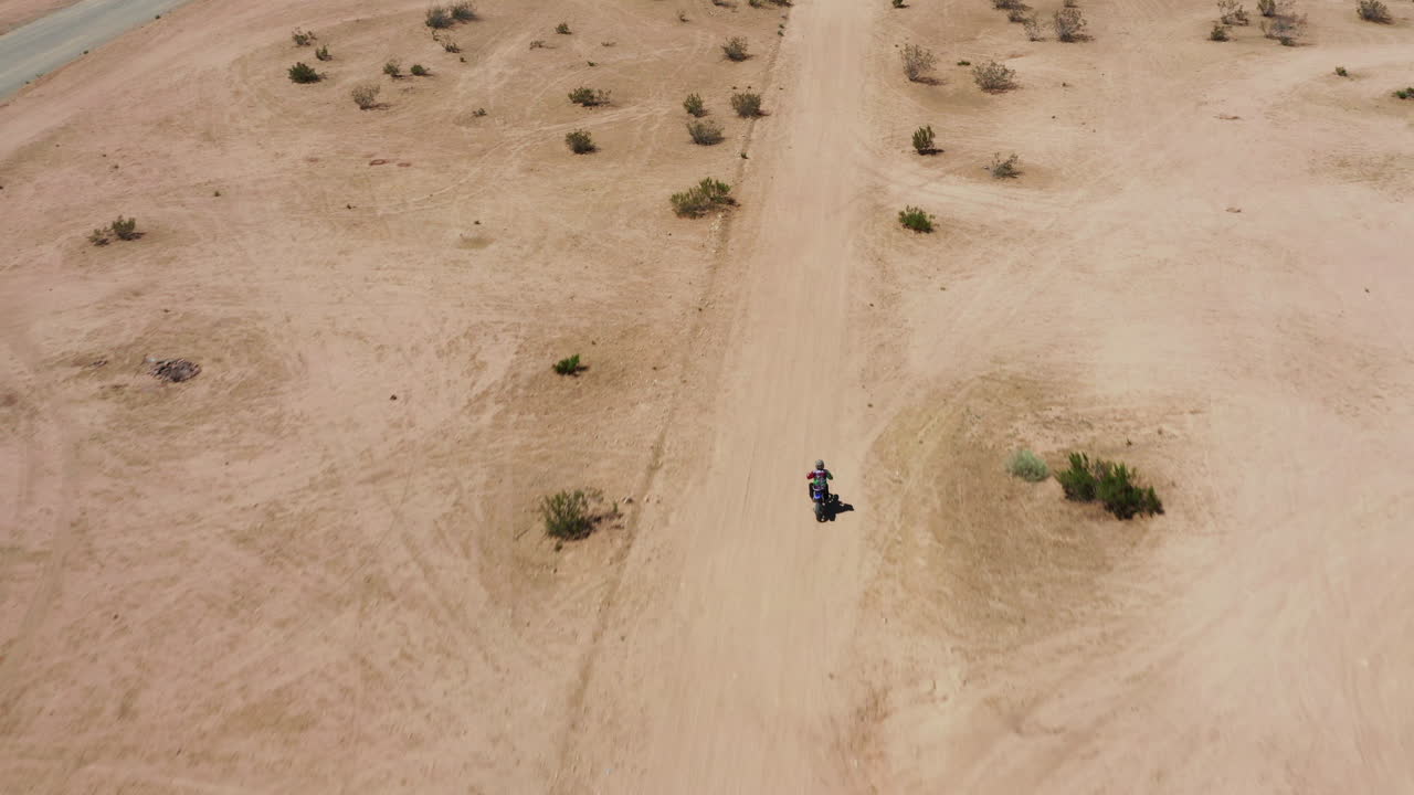 A lone biker riding through the dusty desert land of the Mojave desert in California, an off the grid adventure - Aerial shot