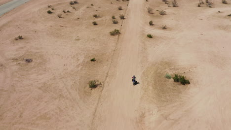 a lone biker riding through the dusty desert land of the mojave desert in california, an off the grid adventure - aerial shot