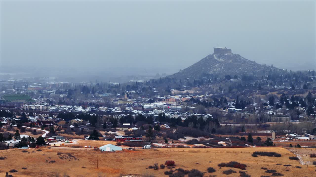 Winterliche Stadtansicht der Kleinstadt Castle Rock, einem Wahrzeichen Colorados. Luftaufnahme mit Drohne: Die schneebedeckte Mesa der Front Range, Autos, Gebäude und Viertel an einem verschneiten, kalten Morgen mit Schneefall und Bewölkung im südlichen Stadtgebiet von Denver.