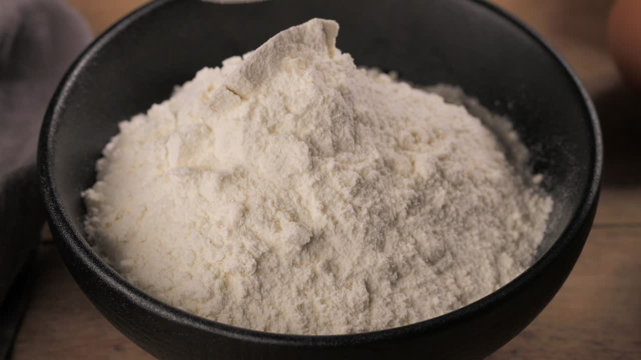 cook puts flour in a bowl with a wooden spoon for making dough