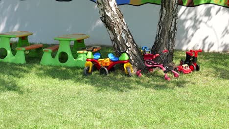 juguetes para montar, camiones mesas de picnic de plástico bajo un árbol debajo de un árbol fuera de la escuela primaria