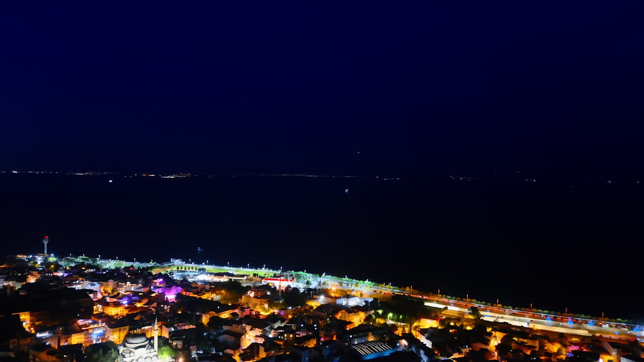 Brightly illuminated city and dark waterscape of the sea. Drone flight over the night scenery of Istanbul, Turkey