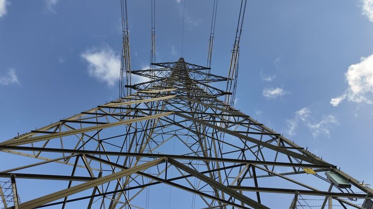 Looking up through the steel lattice of a high voltage transmission tower against blue sky