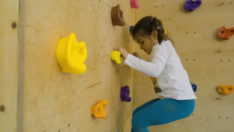 medium shot of a little girl climbing a rock climbing wall