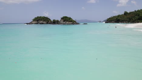 Gorgeous-aerial-wide-shot-of-water-crashing-on-the-beach-shore-sand-two-archipelago-in-distance-blue-sky-white-clouds-turquoise-water-relaxation-vacation-tourism