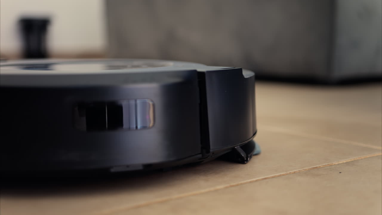 Close up of a black robot vacuum cleaner moving and rotating on the floor tiles