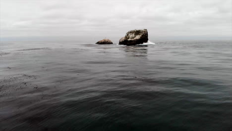 Fly-in-to-guano-covered-bird-rookery-rock-outcropping-in-ocean-on-Central-California-Coast-at-sunset-with-crashing-waves,-drone,-4k-Pro-Res-422HQ