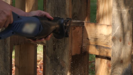 close up of man using reciprocating saw to cut through panel of fence