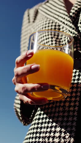close-up of a hand holding a glass of orange drink against a blue sky