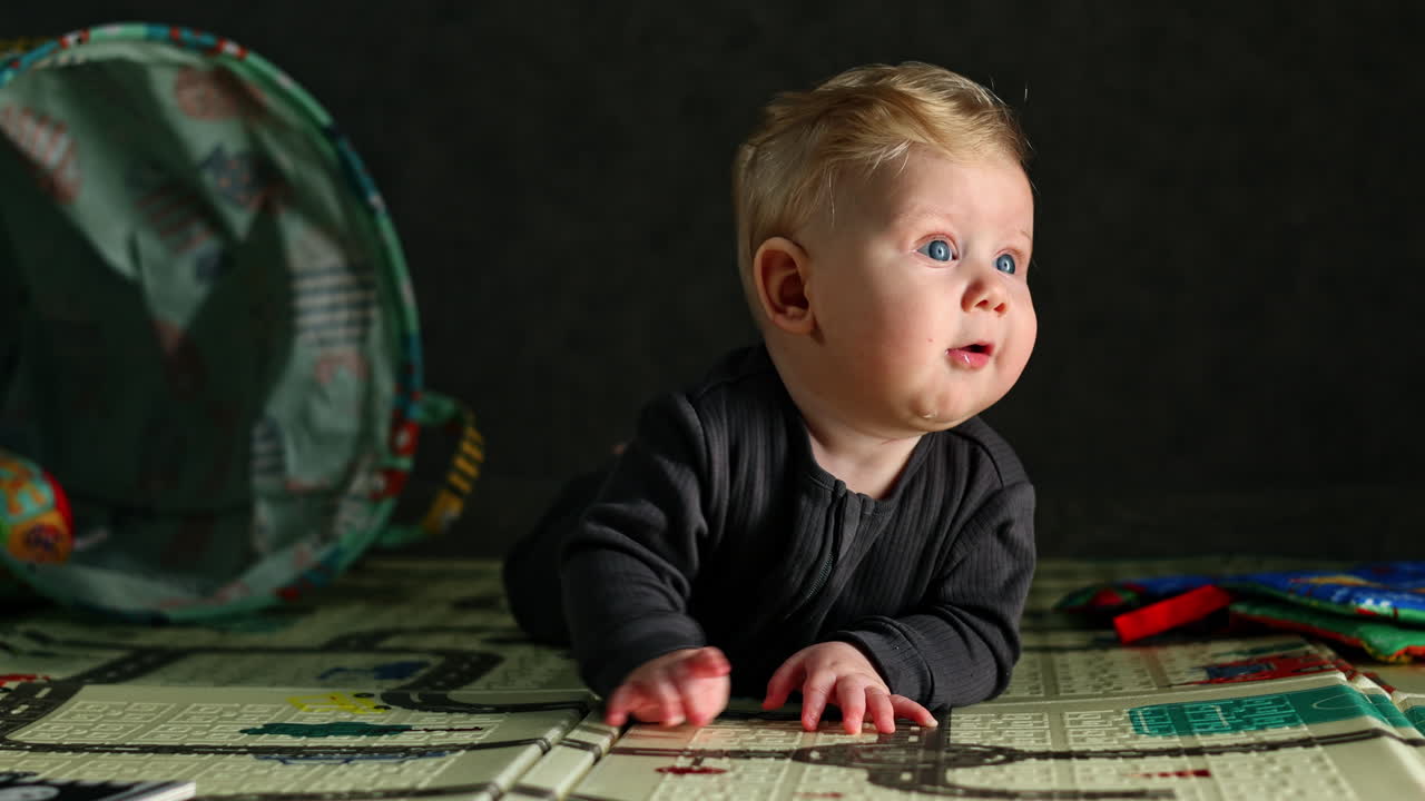 Ein Babyjunge lernt, seinen Kopf zu halten, während er auf dem Boden liegt. Ein kleiner Junge spielt zu Hause auf dem Boden. Das Kind spielt alleine zu Hause. Kindesentwicklung