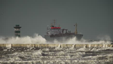 Olas-De-Tormenta-Chocan-Sobre-El-Muelle-De-Cemento-De-Ijmuiden-Con-Un-Barco-Al-Fondo,-Teleobjetivo