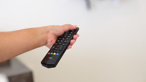 una mano presiona un botón en un control remoto en un entorno brillante y minimalista, sugiriendo la interacción con un dispositivo