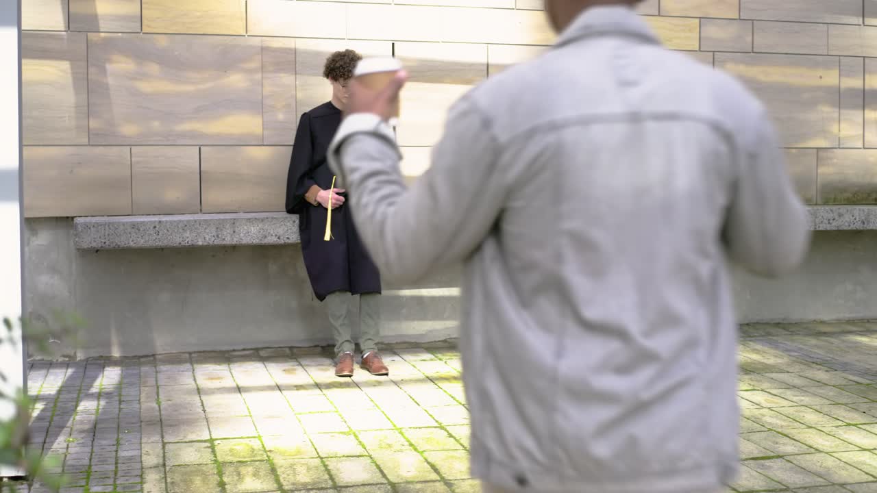 Amici uomini con un cordino giallo che controllano il telefono, mentre un amico arriva con una tazza e uno spuntino da condividere in cortile.