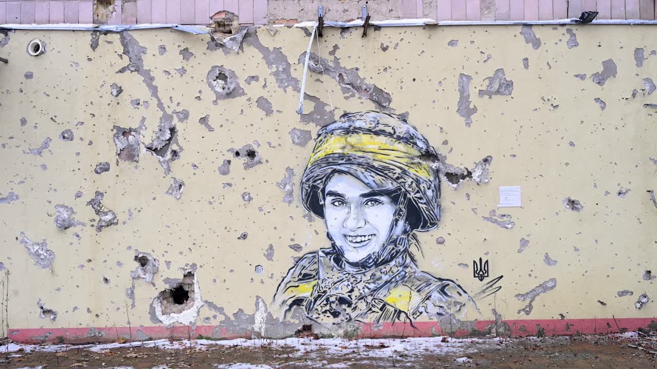 A mural of a Ukrainian soldier, framed by actual bullet and shrapnel holes, on a heavily damaged building in Irpin, Ukraine, during the Ukraine-Russia conflict.