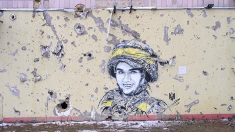a mural of a ukrainian soldier, framed by actual bullet and shrapnel holes, on a heavily damaged building in irpin, ukraine, during the ukraine-russia conflict.