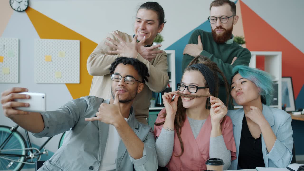 Joyful youth business team taking selfie in office posing with funny gestures having fun