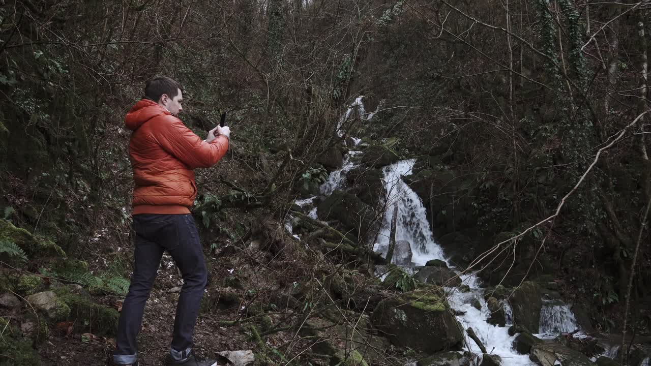 hombre tomando una foto de una cascada en el bosque