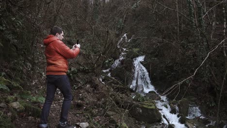 man taking photo of waterfall in forest