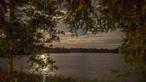 Moon-glowing-while-flow-through-skyscape-and-reflecting-on-lake-water,-fusion-time-lapse