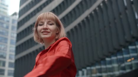 young woman in red jacket in front of city buildings