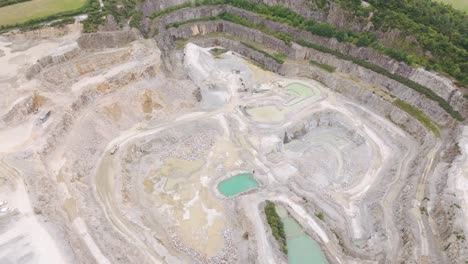 Aerial-view-of-a-truck-driving-down-to-the-bottom-of-an-aggregate-quarry-to-pick-up-fresh-rock,-highlighting-the-scale-of-the-operation