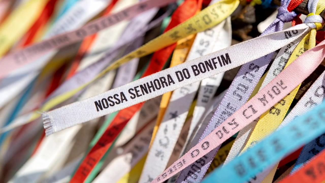Shifting camera keeping white ribbon NOSSA SENHORA DO BONFIM in focus at shrine, showing knots