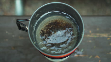 close up overview of travel gas burner and small pot with boiling and steaming hot water at glacier np campground and creek camp site in usa